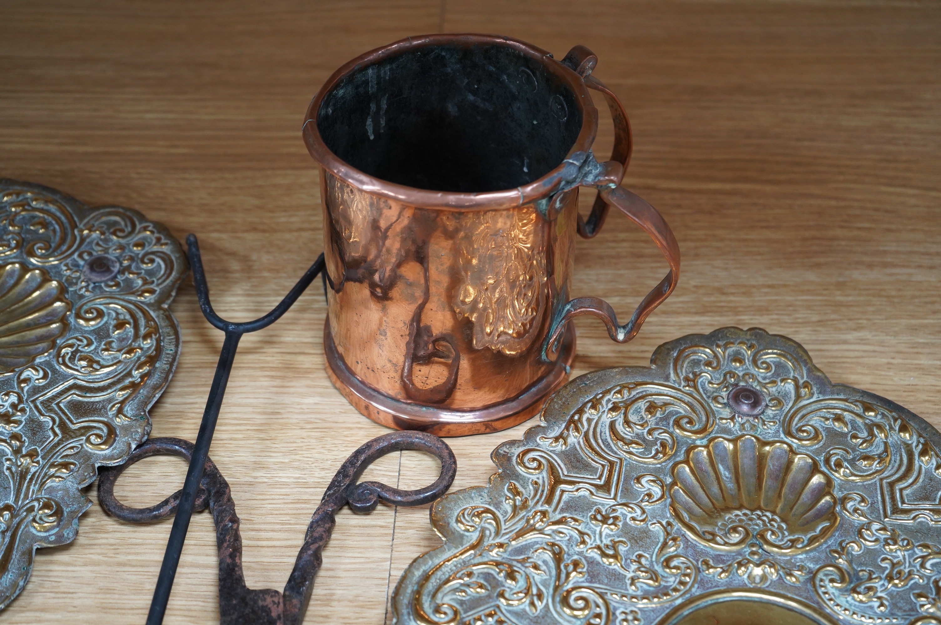 A pair of brass repousse wall sconces, a copper two handle mug, a small brass sun dial, a pair of tongs and a roasting trivet. Condition - poor to fair